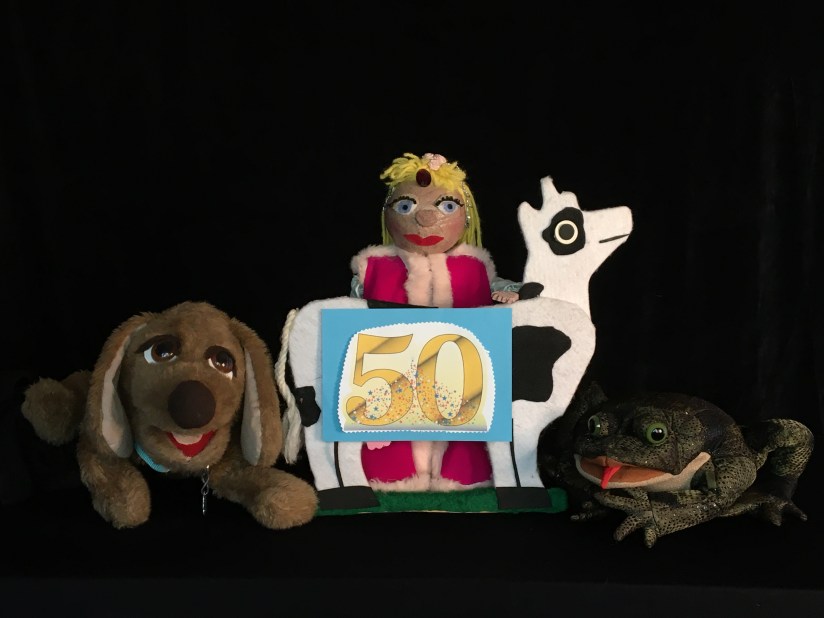 Dog, princess, cow and frog puppets holding a golden 50 sign